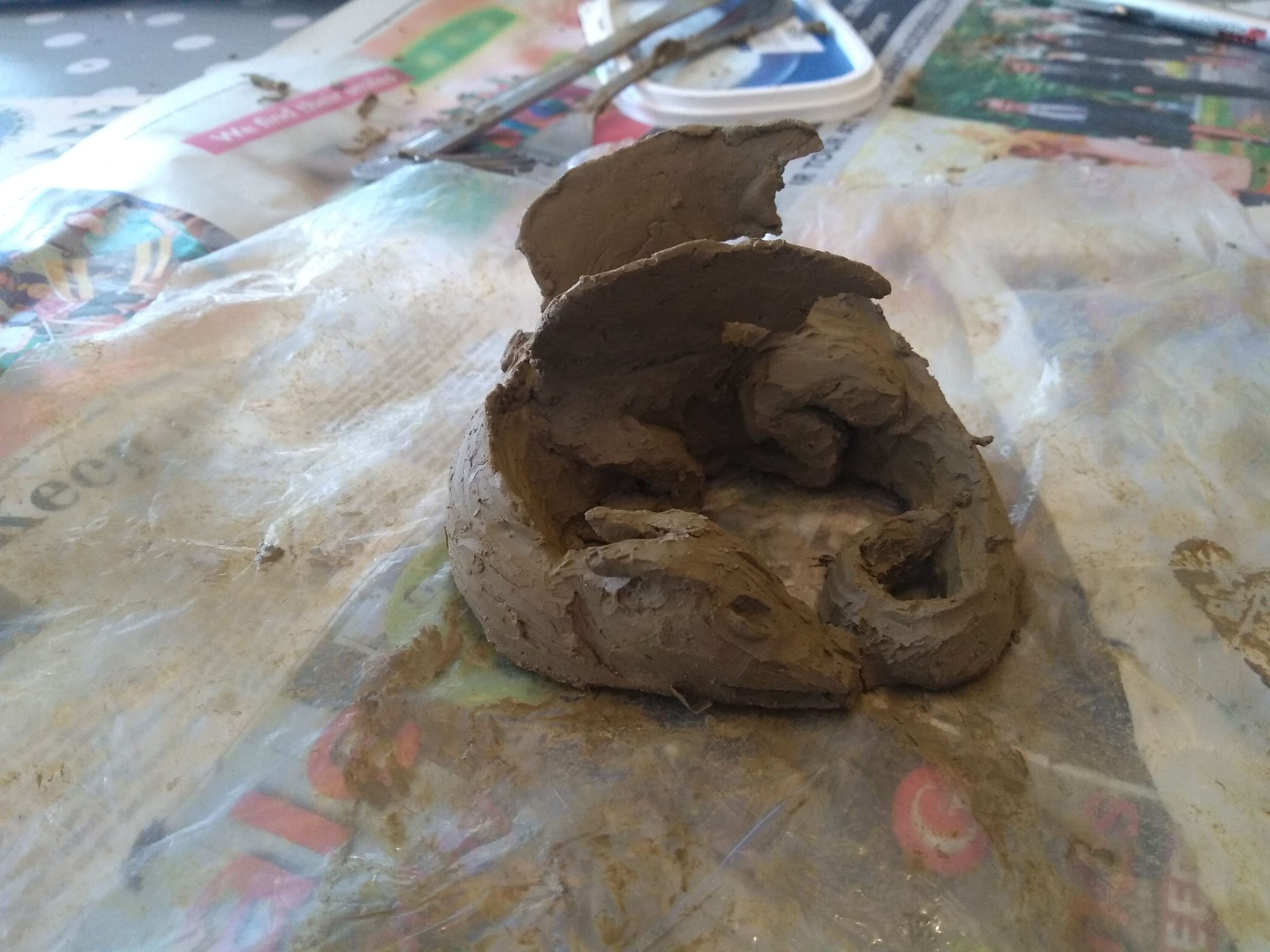 A work in progress clay sculpture of a dragon. Both wings are on the dragon.