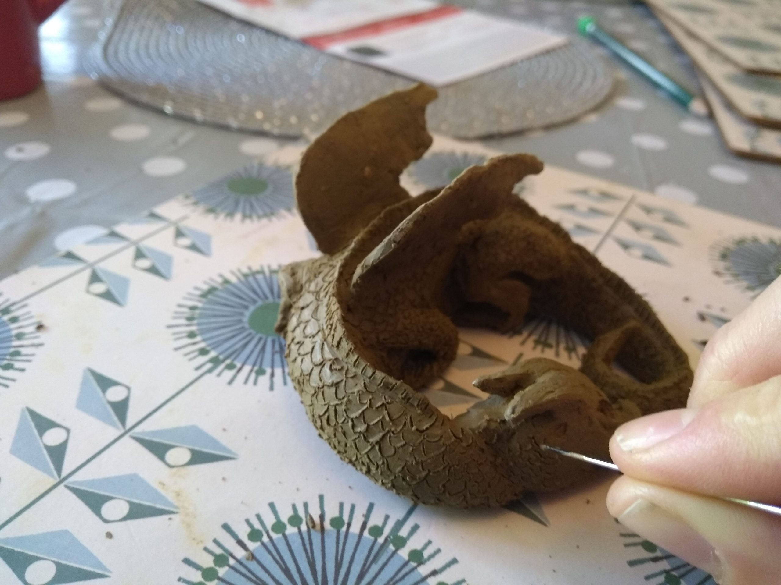 Work in progress photo of a clay dragon, a hand is marking on the dragon scales.